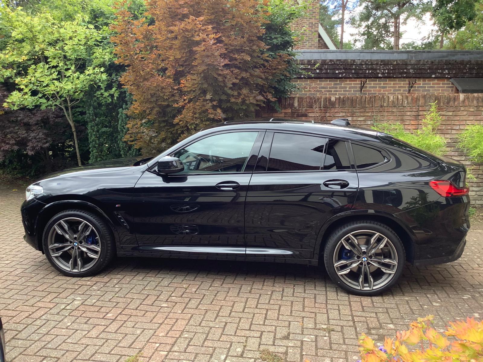Black BMW G02 X4 in side profile on a paved driveway