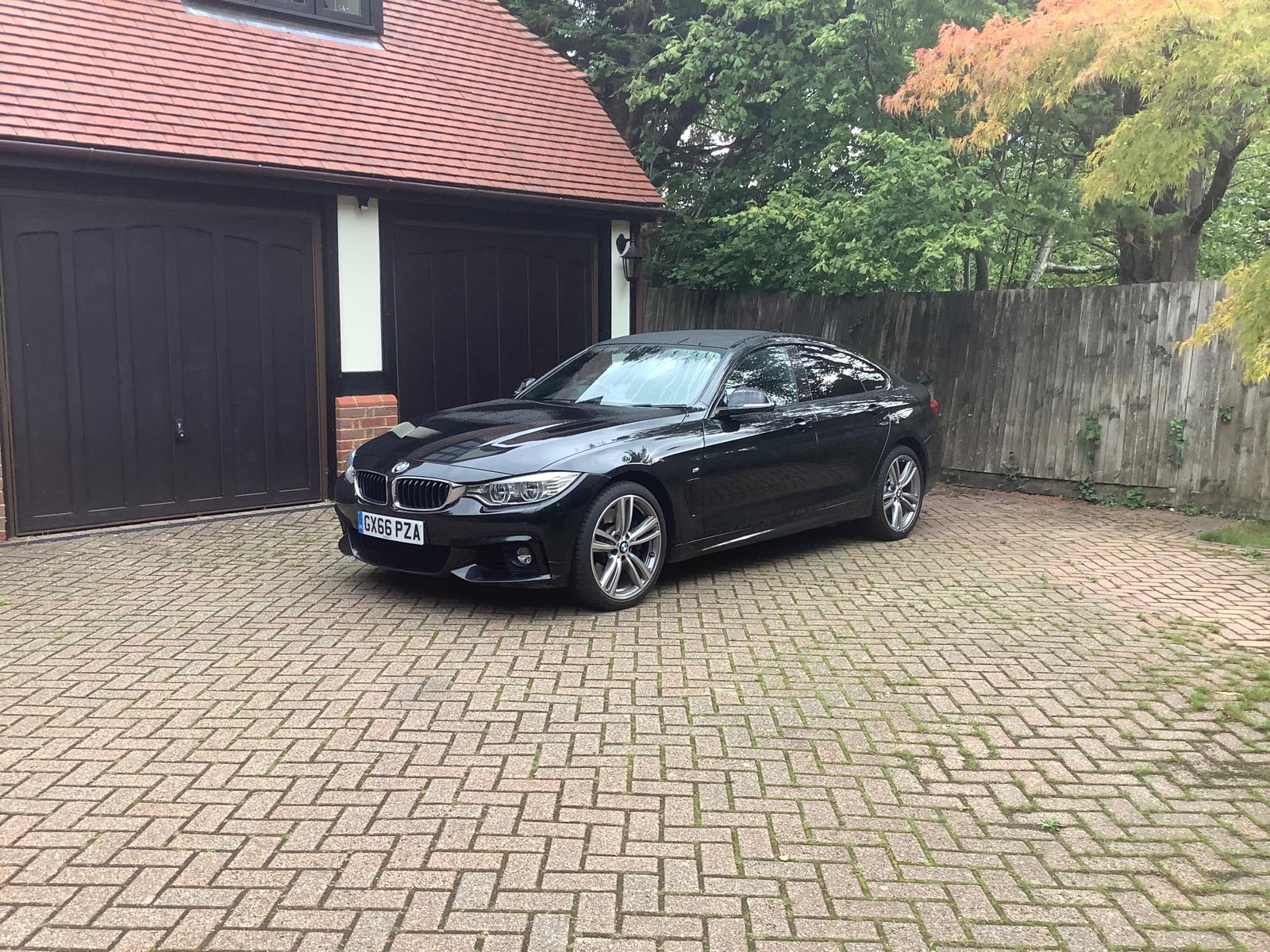 Black BMW 4 Series Gran Coupe parked in front of a garage
